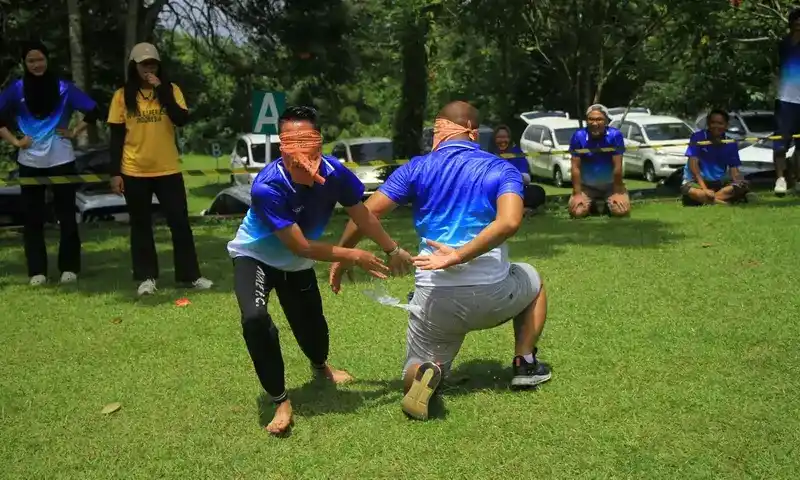 Dua peserta laki-laki sedang berkompetisi dalam game outbound "Gladiator" dengan mata tertutup di lapangan rumput hijau Bogor.