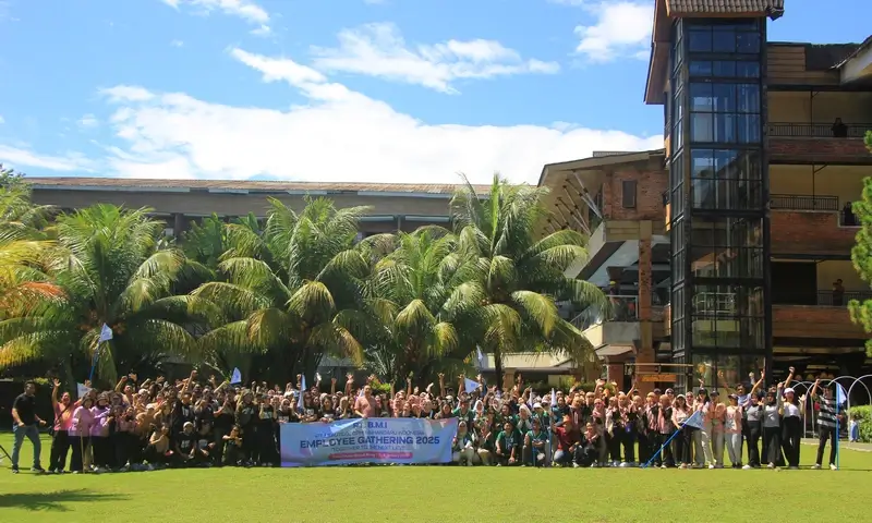 Foto sampul kegiatan BoundEx Indonesia yang menampilkan ratusan karyawan PT BMI (Beautylishopi Mahandaru Indonesia) sedang melakukan sesi foto bersama di lapangan kolosal Grand Mulya Bogor Resort. Peserta terlihat kompak mengenakan seragam hijau dan merah muda, mengangkat tangan dengan antusias. Latar belakang menunjukkan arsitektur gedung Grand Mulya yang megah dengan elemen bata ekspos, lift kaca, pohon kelapa asri, serta langit biru cerah. Di bagian depan terdapat banner bertuliskan "PT BMI Employee Gathering 2025".