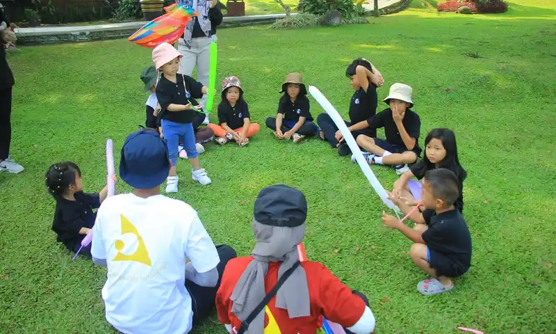 Sekelompok anak-anak duduk melingkar di atas rumput hijau yang asri saat mengikuti sesi kids games dalam acara family gathering di Bogor. Anak-anak tampak antusias memegang balon panjang warna-warni didampingi instruktur BoundEx yang mengenakan kaos putih dan merah.