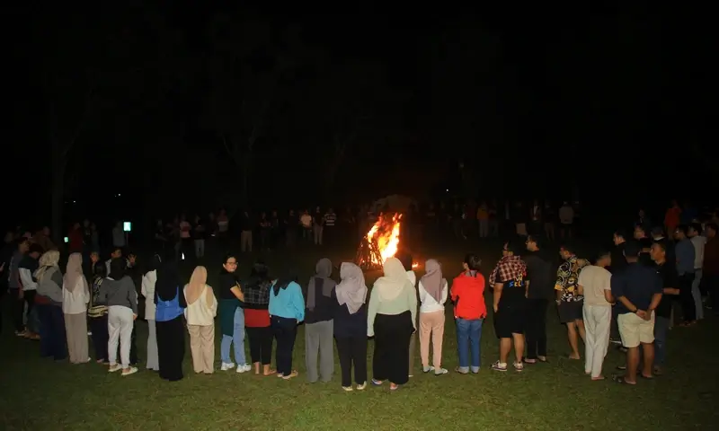 Suasana malam keakraban peserta gathering di Bogor yang berkumpul melingkari api unggun besar untuk sesi refleksi dan hiburan.
