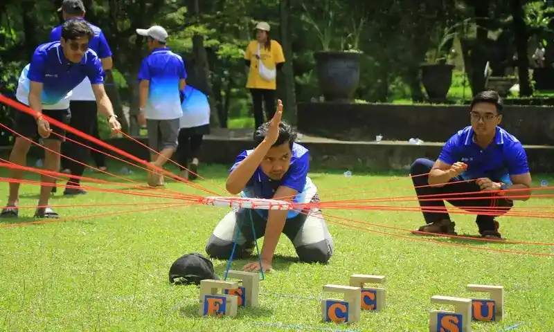 Peserta outbound di Bogor sedang berkonsentrasi penuh menarik tali penyeimbang untuk menyusun balok kayu dalam game Success Tower.