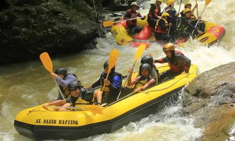 Peserta gathering perusahaan sedang melakukan aktivitas arung jeram (rafting) di Sungai Cisadane, Bogor menggunakan perahu karet kuning dan perlengkapan safety lengkap.