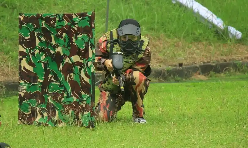 Peserta gathering perusahaan sedang bermain paintball di Bogor dengan seragam loreng dan masker pelindung wajah (goggle) lengkap. Tampak peserta melakukan manuver taktis di balik barikade pelindung dalam simulasi tempur outdoor yang diorganisir oleh BoundEx Indonesia.