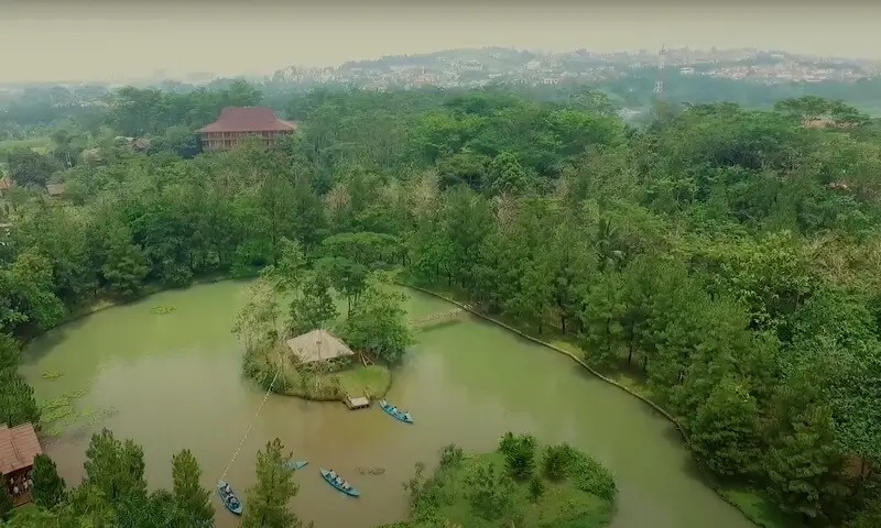 Pemandangan udara danau di Talaga Cikeas Resort Sentul, Bogor. Terlihat beberapa perahu sampan di air, pulau kecil dengan saung di tengah danau, serta dikelilingi pepohonan pinus yang asri, sangat ideal untuk aktivitas outdoor tempat family gathering di Bogor.