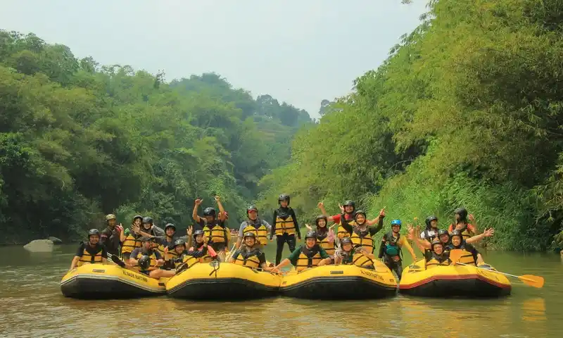 Peserta rafting menggunakan pelampung kuning berpose di atas perahu karet saat family gathering di Bogor di Sungai Cisadane.