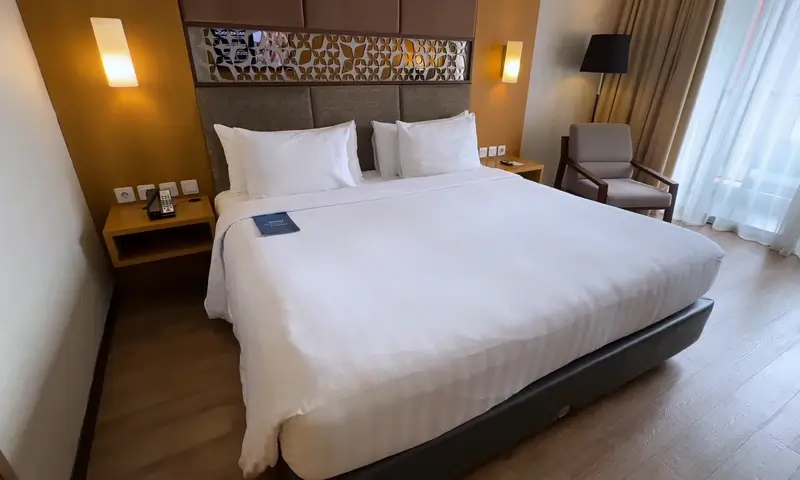 Interior kamar Aston Lake Sentul dengan tempat tidur besar kursi meja samping dan pencahayaan hangat