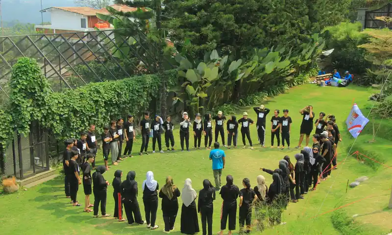 Fasilitator memandu peserta berdiri melingkar saat briefing awal fun games outbound di area rumput Puncak Bogor