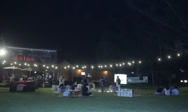 Peserta family gathering perusahaan beraktivitas di halaman resort Puncak dengan latar bangunan penginapan pada malam hari.