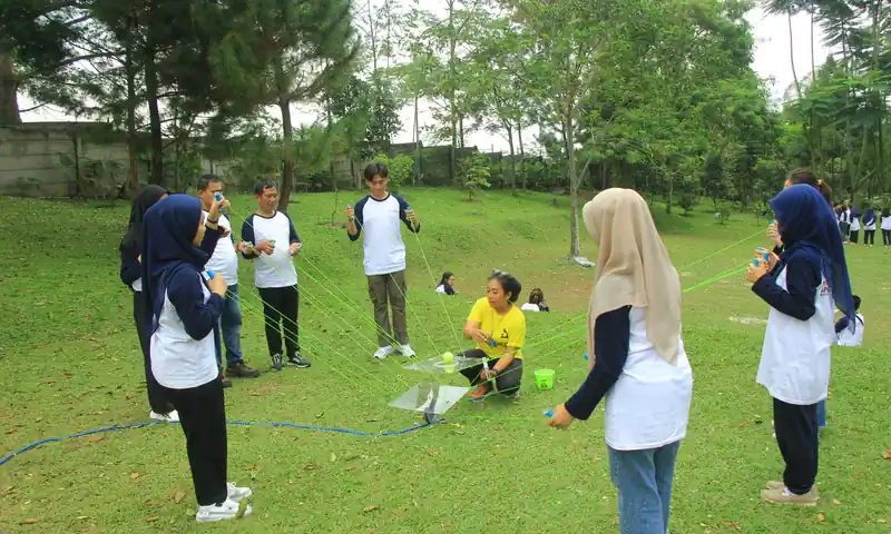 Tim perusahaan menjalankan problem solving games outbound Puncak dengan tali koordinasi.