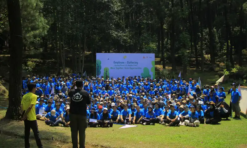 "Peserta employee gathering perusahaan berkaus biru mengikuti sesi kebersamaan di area hutan pinus Bogor dengan backdrop acara.