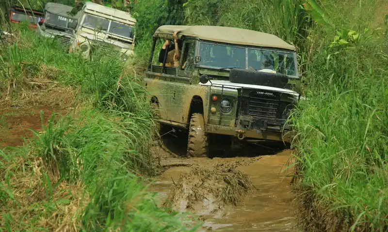 Kendaraan Land Rover melintasi jalur offroad berlumpur di Bogor sebagai bagian dari aktivitas outing perusahaan.